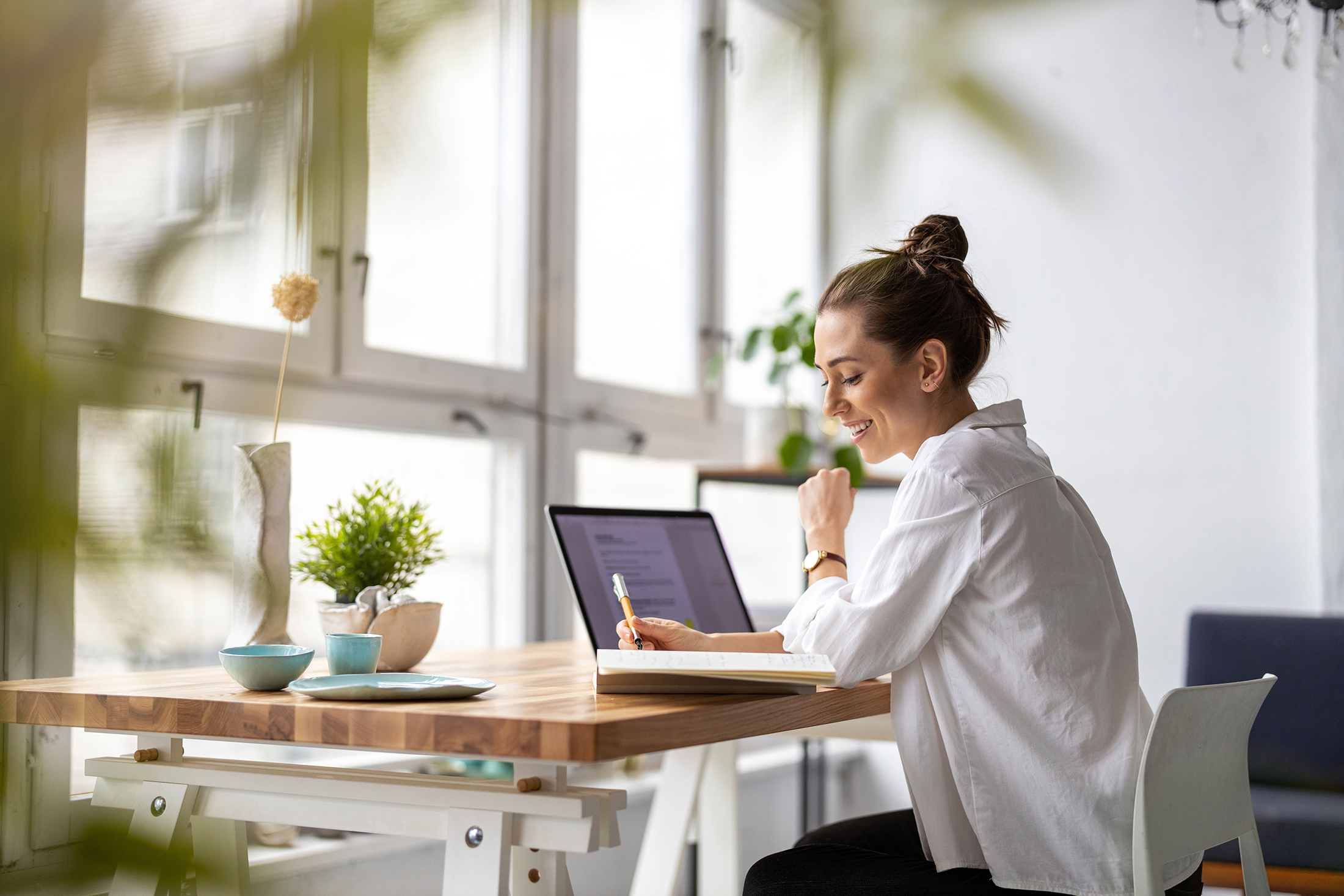 Employee working from home at a table reviewing documents and using a laptop